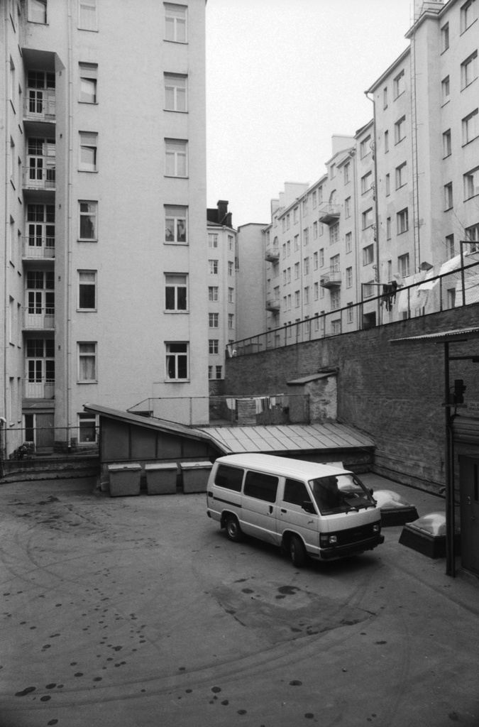 Kirjatyöntekijänkatu. Näkymä Kirjatyöntekijänkatu 8:n pihalta kaakkoon. Pihalla autoja ja roskalaatikoita. Vasemmala Kirjatyöntekijänkatu 6:n talo. Oikealla ylätasanteella Kristianinkadun taloja.