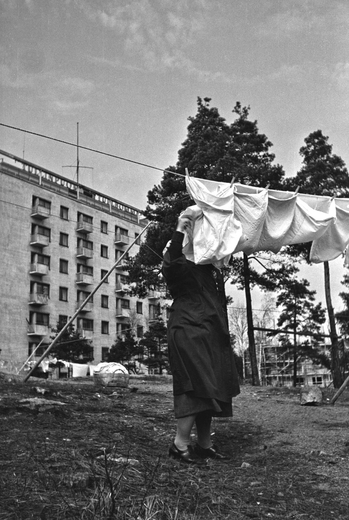 Nainen ripustaa pyykkejä narulle kuivumaan. Taustalla Mannerheimintie 118.