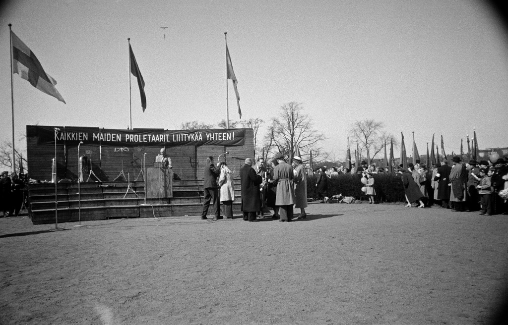 Työväen vappujuhla Kaisaniemessä. Esiintymislava jonka yllä Suomen, Neuvostoliiton ja Ruotsin liput sekä teksti "Kaikkien maiden proletaarit, liittykää yhteen!".