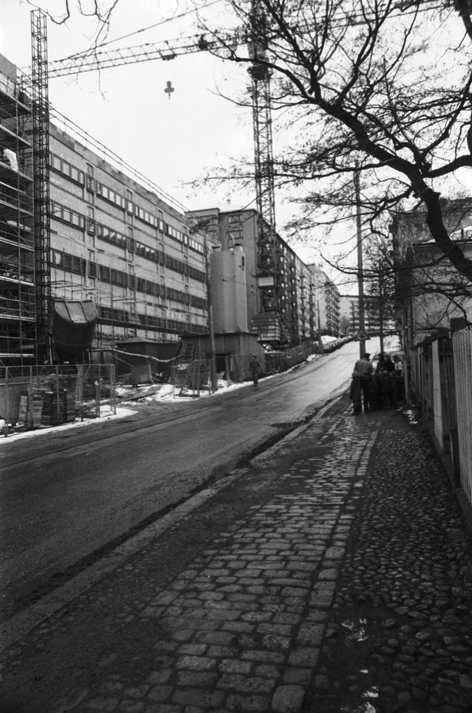 Wallininkatu 2. Vironniemen päiväkodin lapsia ja aikuisia Wallininkatu 3:n (1:n) talojen edustalla katselemassa kadun vastakkaisella puolella rakenteilla olevaa Suomen Kaupunkiliiton toimitaloa (Kuntataloa). Näkymä Ensi linjan suunnalta koilliseen.