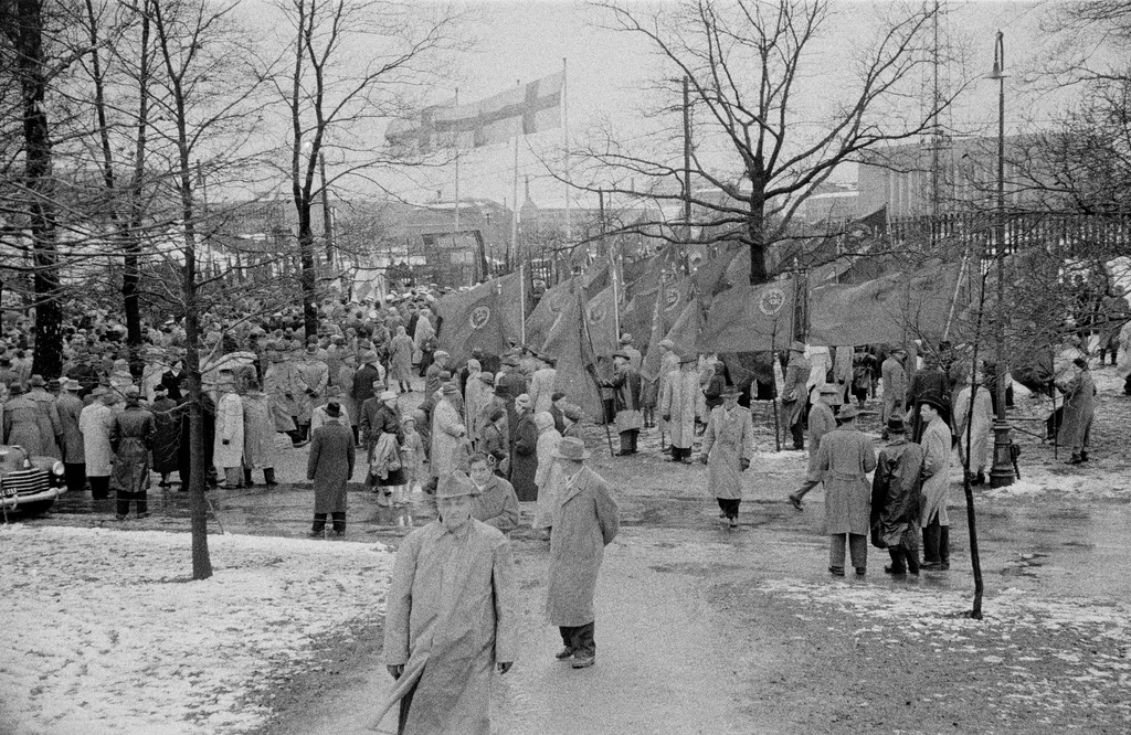 Työväen vappujuhla lumi- ja räntäsateessa Kaisaniemen kentällä 1957. Keskellä Suomen Kommunistisen Puolueen (SKP) lippujen kantajia.