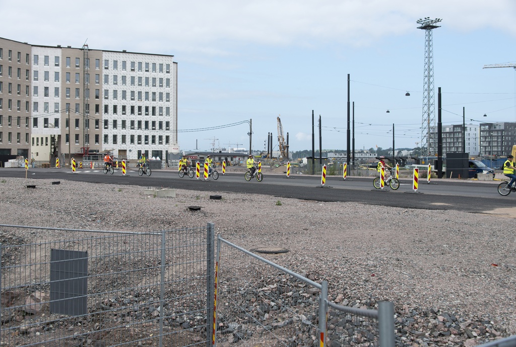 Jätkäsaaren dokumentointi. Vasemmalla Atlantinkatu 7. Oikealla takana Saukonpaadenrannan asuintaloja. Tilapäisiä katujärjestelyjä. Turistiryhmä pyöräilee kadulla.