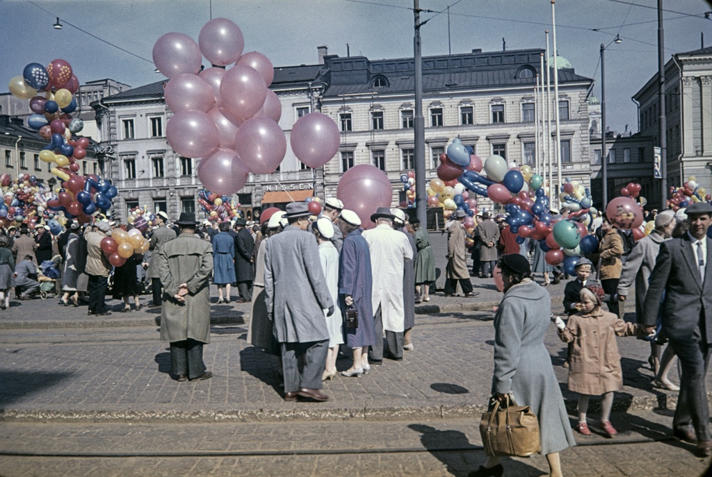 Ilmapallojen myyjiä ja ihmisiä Kauppatorin vapputorilla. Taustalla Pohjoisesplanadi 17 ja 15.