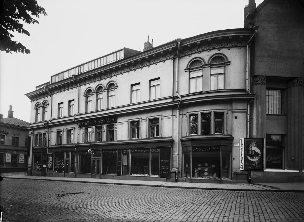 Eteläinen Esplanaadikatu 20. Rakennuksessa on Cafe, Kahvila ja Konditoria K. M. Brondin o.y (myyjä näkyy heikosti ikkunan läpi). Oikealla on Begrafningsbyrå -mainos ja sen vieressä liike Hautaustoimisto. Arkkitehdit Valter Jung ja Emil Fabritius piirsivät talon, joka valmistui 1910-luvulla. Talo purettiin 1972.