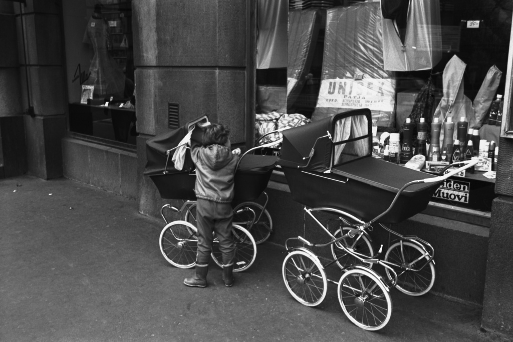 Hämeentie 10. Pieni lapsi sekä kahdet lastenvaunut näyteikkunan edustalla muovituotteita myyvän kivijalkaliikkeen ulkopuolella Hämeentiellä.
