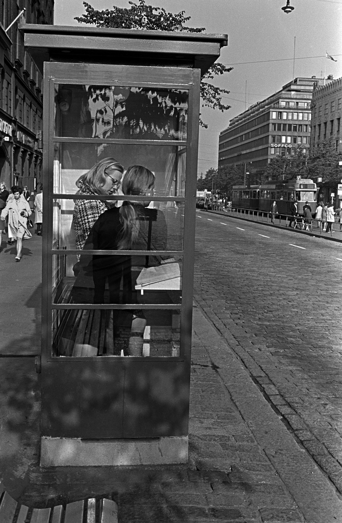 Kaksi tyttöä puhelinkopissa ja jalankulkijoita Mannerheimintiellä Bio Capitolin edessä.