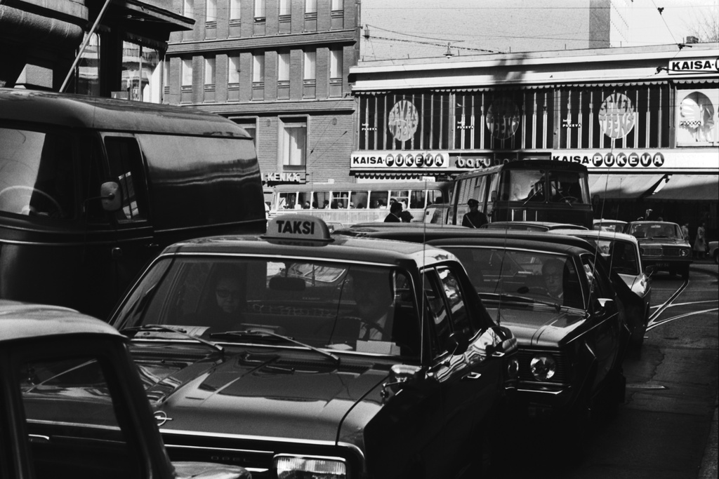 Kaisaniemenkadun suunnalta tulevaa iltapäivän ruuhkaliikennettä Vilhonkadulla. Etualalla taksi (Opel Rekord), sen takana Rambler Hornet -henkilöauto. Taustalla Kaisa-Pukevan tavaratalo.