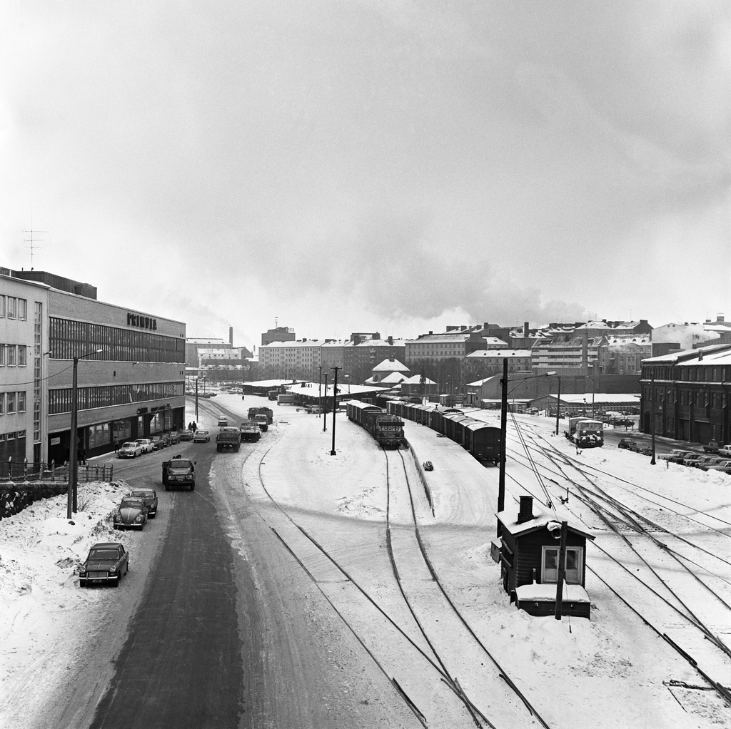 Vallilan teollisuusalue kuvattuna sillalta Sturenkadun ja Teollisuuskadun risteyksessä. Vallilan tavara-asema ja Satamarata. Vasemmalla Teollisuuskatu 3, jossa on Primulan leipomo. Oikealla Satamaradankatu 3. Taustalla vasemmalta alkaen: Aleksis Kiven katu 4, 8, 10, 12, 14, 16, 18. Vasemmalla puolella pysäköidyt autot etualalta lukien: Triumph Herald, Volkswagen, kaksi Volvo Amazonia,  Volvo 164, Volvo Amazon, Volkswagen ja Volvo Amazon. Tiellä liikenteessä ajaa Bedford -kuorma-auto, Ford Cortina sekä Peugeot 404.