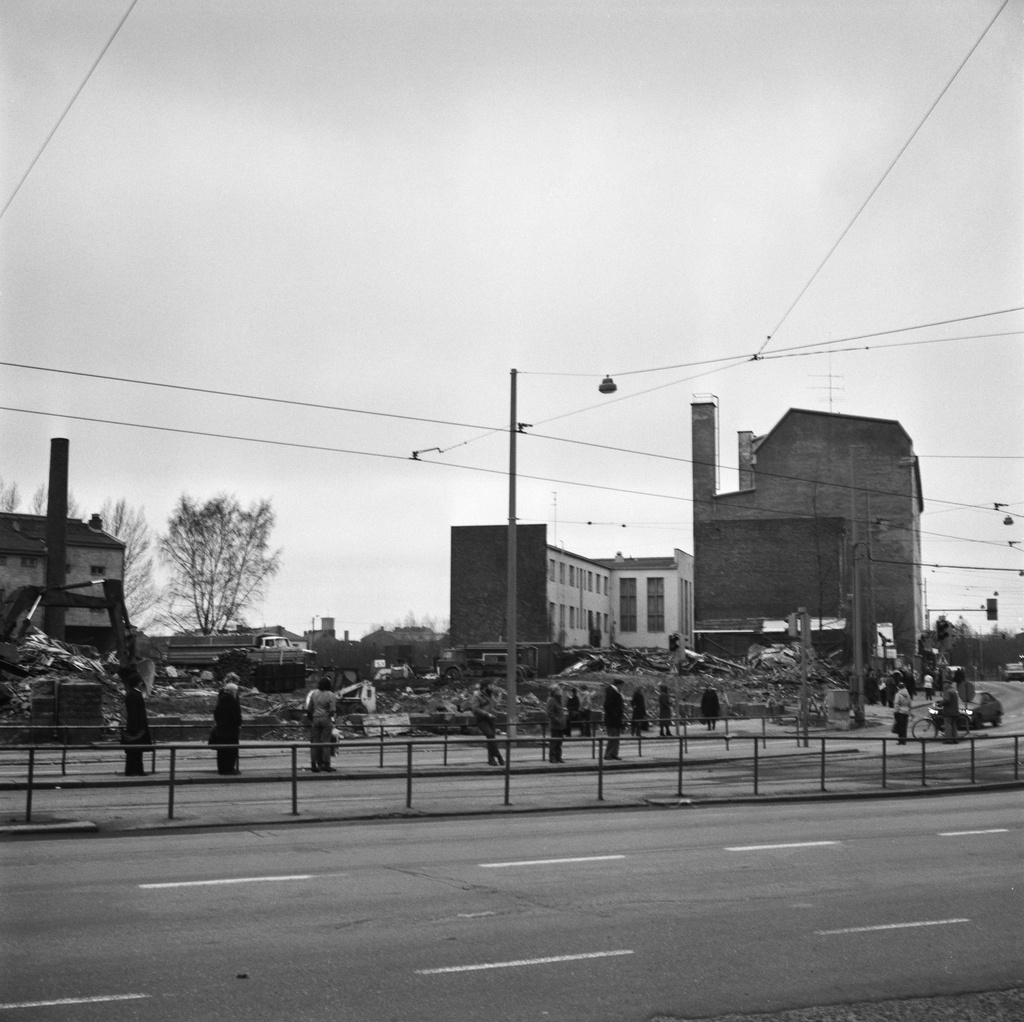 Purkutyömaa Hämeentie 58:ssa. Ihmiset odottavat raitiovaunua.