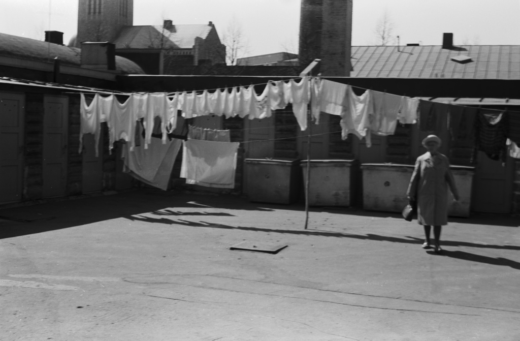 Kaarlenkatu 3. Näkymä Kaarlenkatu 3:n pihapiiristä. Narulla pyykkejä kuivumassa sekä jäteastioita matalan piharakennuksen edustalla. Taustalla Kallion kirkko.