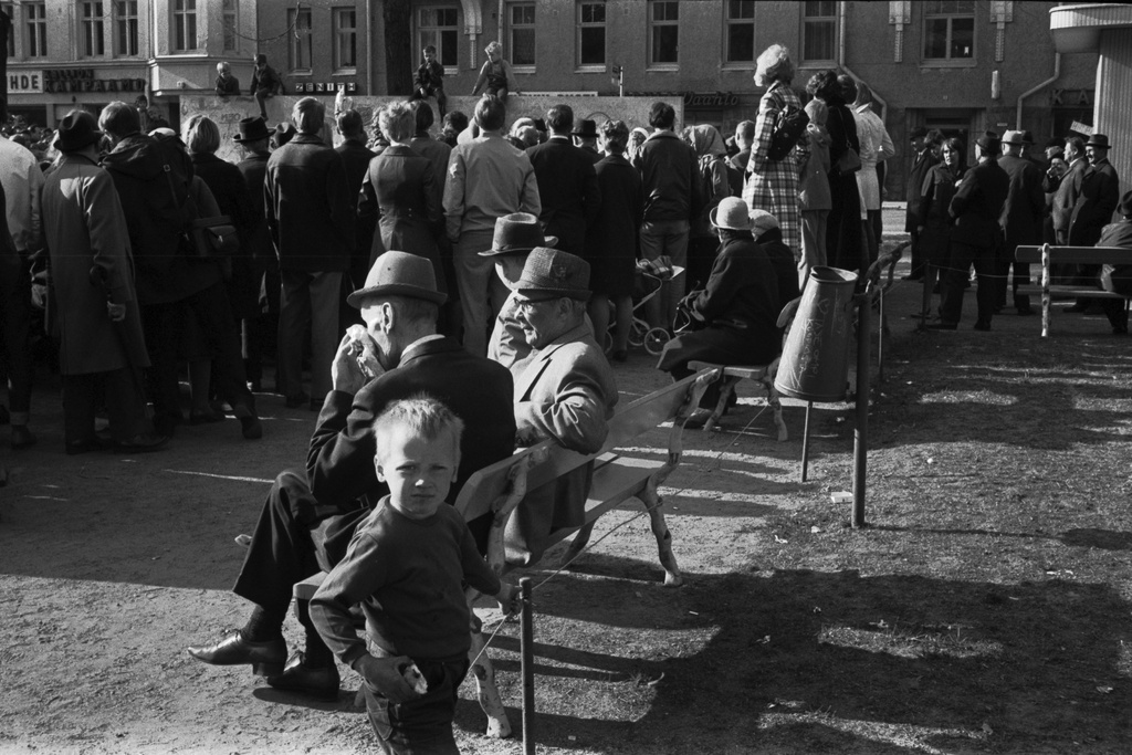 Karhupuisto. Helsingin juhlaviikot. Eri ikäisiä ihmisiä seuraamassa esitystä Karhupuistossa puistotapahtuman aikaan. Etualalla penkeillä istuvia, taaempana penkillä seisovia ihmisiä.