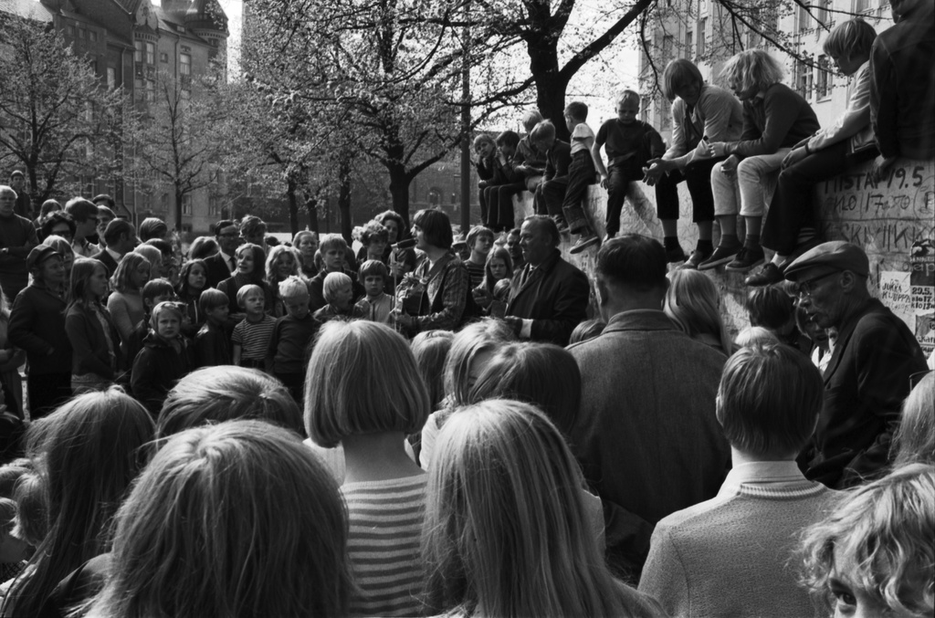 Karhupuisto. Helsingin juhlaviikot. Jukka Kuoppamäki lavalla aloittamassa esiintymistä runsaslukuiselle yleisölle Karhupuistossa järjestetyssä puistotapahtumassa. Lavalla myös kaksi puistojen miestä.