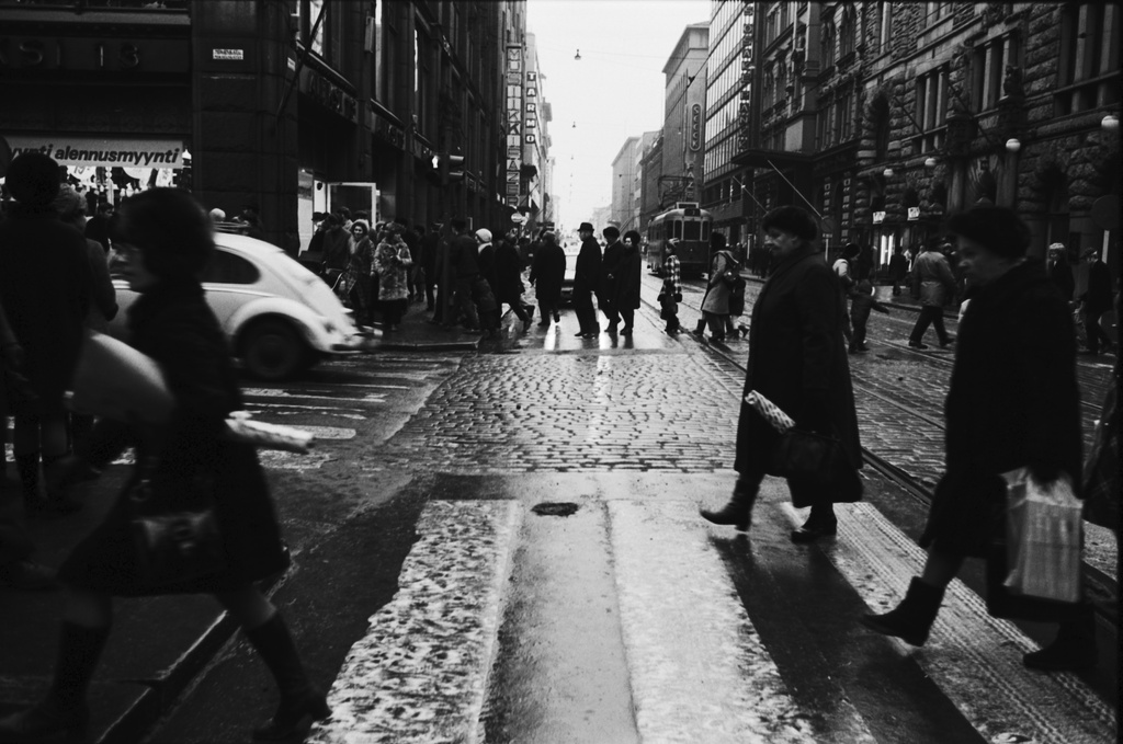 Kluuvi, Aleksanterinkatu. Aleksanterinkadun kävelykatukokeilu (12.6.1970-8.1.1971) on päättynyt. Jalankulkijoita ja ajoneuvoliikennettä Aleksanterinkadun ja Mikonkadun kulmassa puolen päivän aikaan. Näkymä Senaatintorin suuntaan.