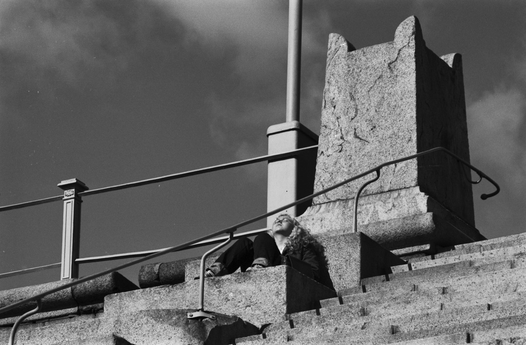 Hallituskatu 7. Nuori nainen ottamassa aurinkoa Tuomiokirkon portaiden laidalla ylätasanteella olevan kivipylvään juurella.