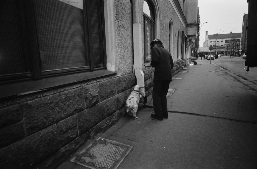 Taka-Töölö, Sibeliuksenkatu. Mies ja koira Sibeliuksenkatu 7:n talon seinustan vierellä. Näkymä Mannerheimintien suuntaan, taustalla Messuhalli (nyk. Töölön kisahalli).