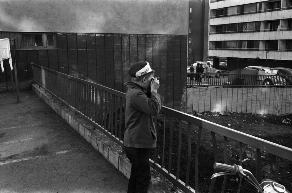 Neljäs linja 17, 19. Poika valokuvaamassa Neljäs linja 17:n talon päädystä länteen. Etualalla Castréninkatu 11 tonttia. Taustalla oikealla lapsia sekä autoja Neljäs linja 19:n talon edustalla.