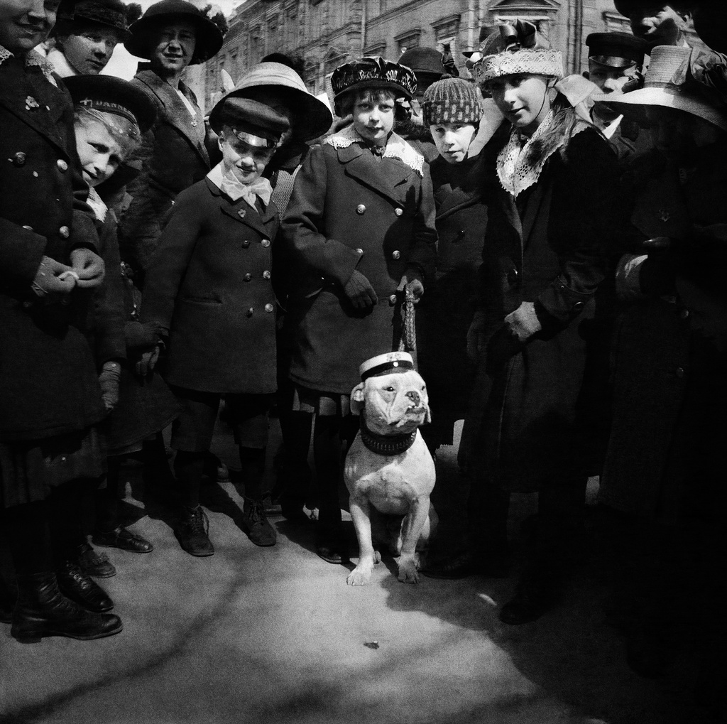 Lapset ja koira viettävät vappua Kauppatorilla Pohjois-Esplanaadikatu (Pohjoisesplanadi) 17:n edustalla. Kuva on julkaistu Veckans Krönikassa 9.5.1914. Kuvatekstissä koiraan viitattiin luonnehdinnalla ?också en ?civis academicus??