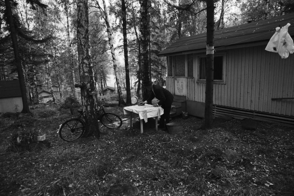Kulosaari Näkymä syksyiseltä Kivinokan kesämaja-alueelta. Mökin pihalla mies pesemässä juuriharjalla pöydän päälle levitettyjä pitkiä alushousuja. Koivunrunkoa vasten nojaa miesten polkupyörä.