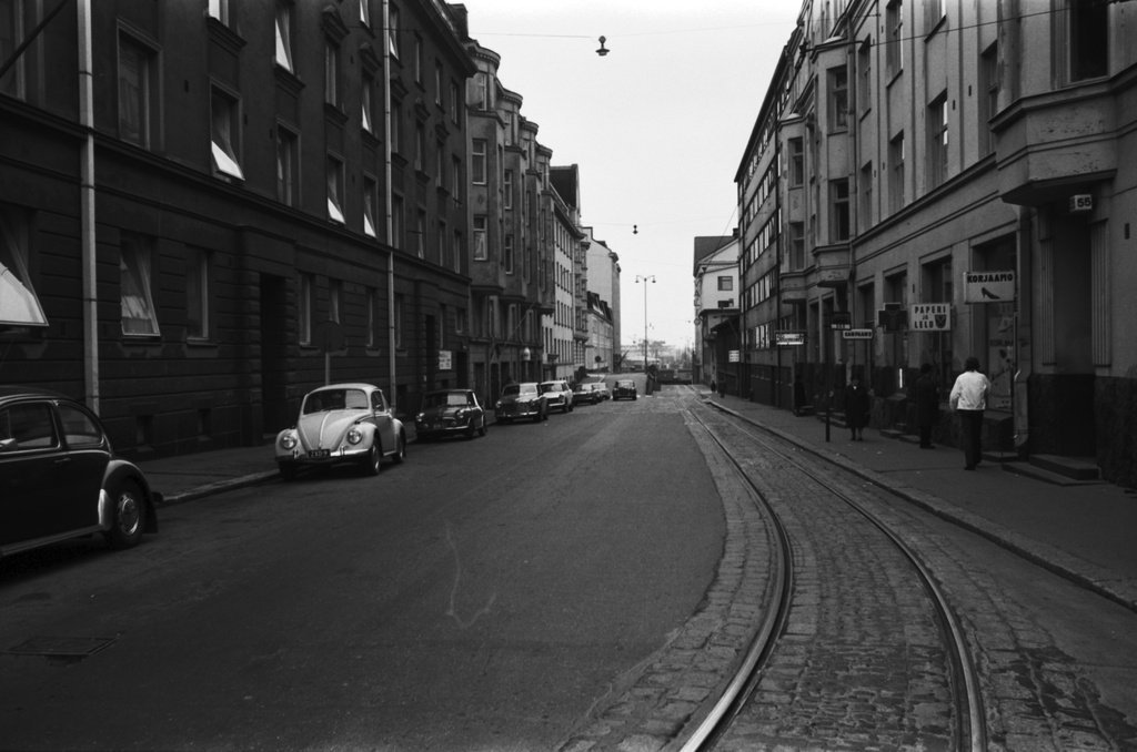 Näkymä Kalevankadulta Hietalahdenkadun kulmasta lounaaseen, Hietalahdenrannan suuntaan. Vasemmalla pysäköityjä autoja, oikealla jalankulkijoita liikkeiden ikkunoiden edessä.