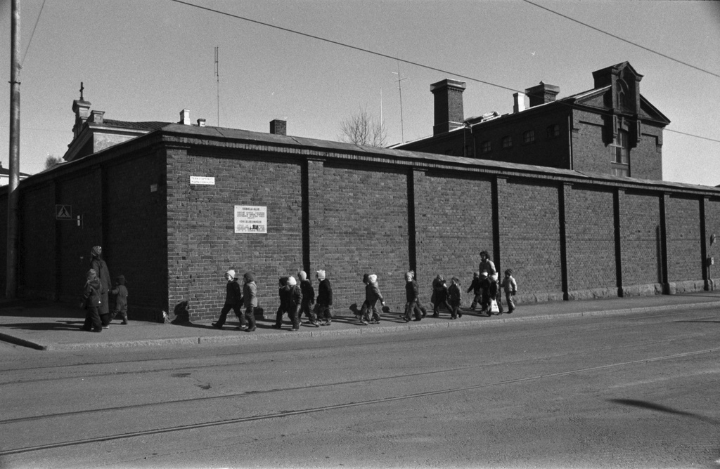 Linnankatu. Vironniemen päiväkodin lapsia ja aikuisia kävelemässä Katajanokan vankilan muurin vierustalla Vyökadun kulmassa Katajanokan tutustumiskierroksella. Tutustuminen Katajanokan vanhoihin ja uusiin rakennuksiin liittyi päiväkodissa kevätkaudella toteutettuun Viihtyisä ympäristö -projektiin.