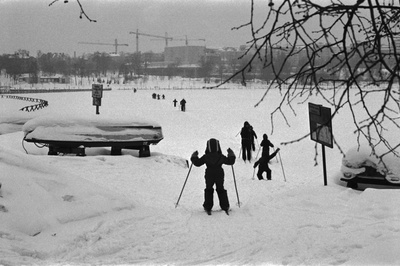 Kaisaniemenranta. Vironniemen päiväkodin lapsia ja aikuisia hiihtämässä Kaisaniemenrannasta Kaisaniemenlahden jäälle kohti Tokoinrantaa. Jäällä vasemmalla aita. Taustalla vasemmalla Cafe Piritta, keskellä Helsingin kaupunginteatteri.  similar photo