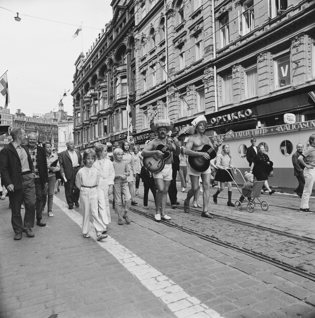 Kävelykatukokeilun avajaiset Aleksanterinkadulla Helsinki-päivänä 1970.. Keihäsmatkat -matkatoimiston mainostempaus. Kävelykatukokeilu toteuttiin  Aleksilla 12.6.1970-8.1.1971. Kitaransoittajina Esko Toivonen alias Eemeli ja Tapio Rautavaara.