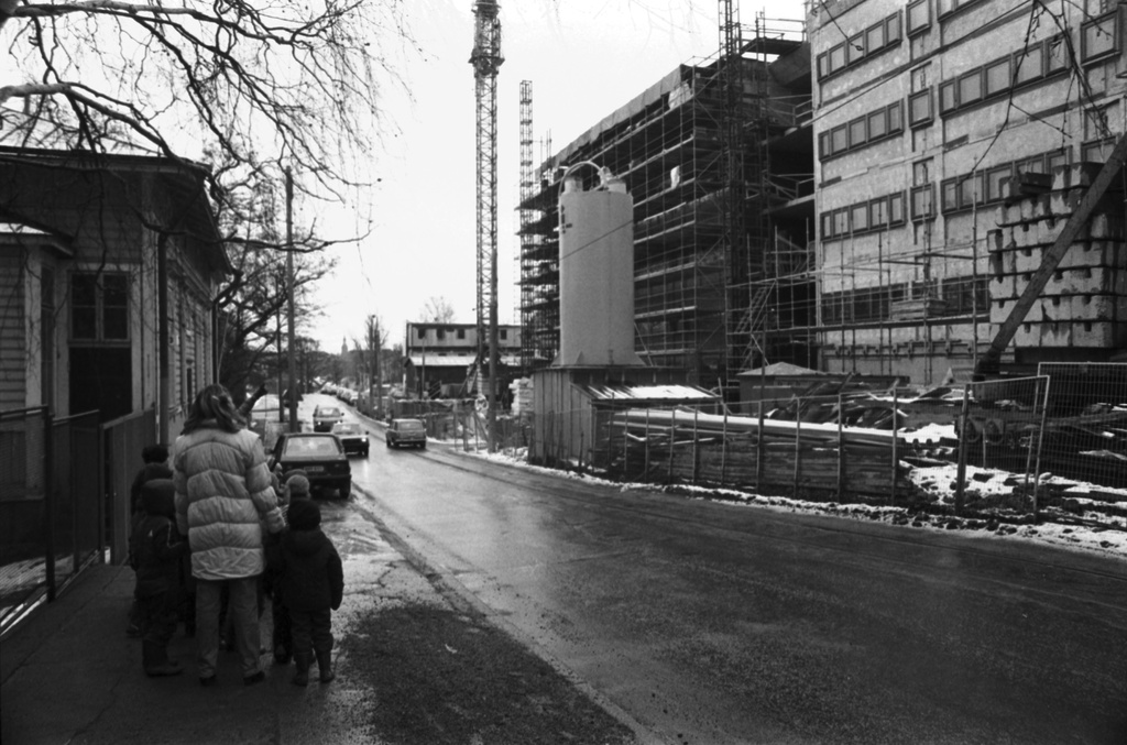 Wallininkatu 2. Vironniemen päiväkodin lapsia ja aikuisia Wallininkadulla matkalla tutustumaan oikealla olevan Suomen Kaupunkiliiton toimitalon (Kuntatalon) rakennustyömaahan. Vasemmalla Wallininkatu 3:n (1:n) puutalo.