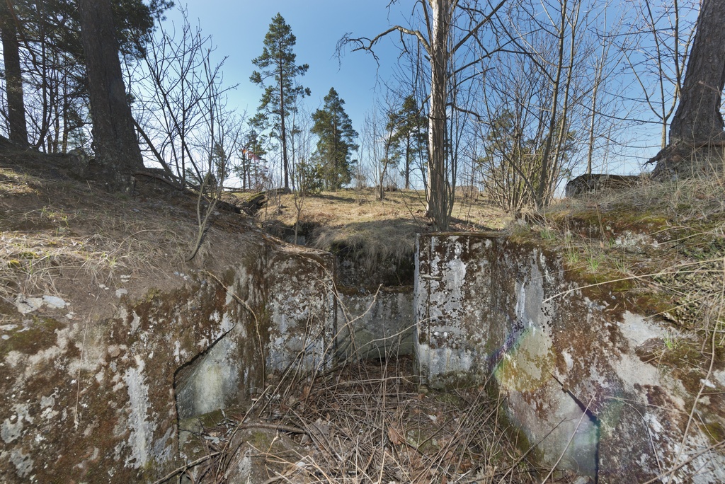 Länsimäki. Ensimmäisen maailmansodan aikainen maalinnoitus, puolustusasema II:8 Länsimäessä, Vantaalla. Kuvassa on kallioon louhittu betoninen konekivääriasema aseman pohjoisosassa. Vasemmalla seinällä näkyy konekiväärin jäähdytysvesisäiliötä varten tehty komero. Oikealla seinällä on toinen, pienempi komero, jonka tarkoitusta ei tiedetä. Katto on räjäytetty, mutta seinät ja oviaukko ovat ehjät. Oviaukon edessä ja  aseman pohjalla on räjähdyksestä syntyneitä betoninpaloja. Kuvaussuuntana etelä.