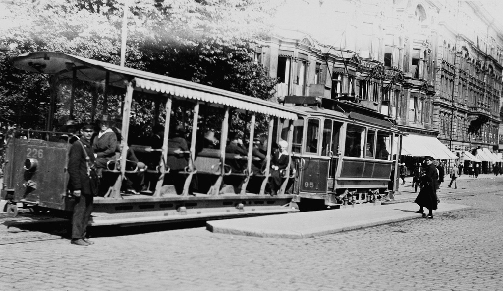 Raitiovaunu avoperävaunuineen Aleksanterinkatu 21:n kohdalla. Taustalla City Passagen ja Husqvarnan liike.