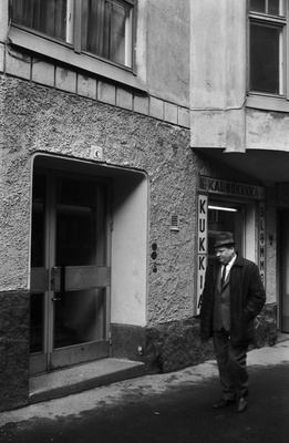 Liisankatu 9. Mies kävelemässä Liisankatu 9:n jugendtalon edustalla. Vasemmalla C-portaan ulko-ovi, oikealla kukkakauppa Kaunokukan näyteikkuna.  similar photo