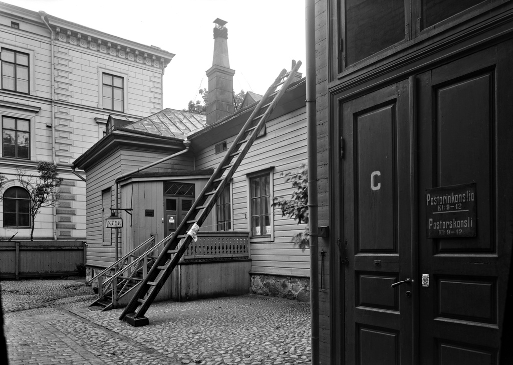 Annankatu 14 - Bulevardi 16, näkymä sisäpihalta. Oikealla Helsingin ruotsalais-suomalaisen seurakunnan pastorinkanslian sisäänkäynti. Vasemmalla sisäänkäynti Kristliga Föreningen av Unga Män (Nuorten miesten kristillinen yhdistys) -yhdistyksen tiloihin. Katolle vieviin tikkaisiin nojaa mahdollisen tulipalon sammuttamisessa käytettävä palohaka. Taustalla on Svenska Fruntimmerskolanin eli ruotsalaisen tyttökoulun rakennus osoitteessa Bulevardi 18-20, jossa nykyään toimii Helsingin eurooppalainen koulu. Vuodelta 1885 olevan koulurakennuksen suunnittelijat ovat Ludvig Isak Lindqvist ja Magnus Sjerfbeck.