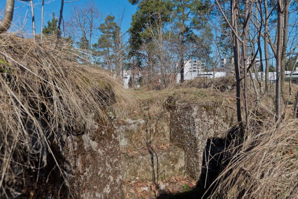 Länsimäki. Ensimmäisen maailmansodan aikainen maalinnoitus, puolustusasema II:8 Länsimäessä, Vantaalla. Kuvassa näkyy kallioon louhittua, betonilla tuettua taisteluhautaa sekä hautaan johtavat betoniset kolmeaskelmaiset portaat. Aseman pohjoisosaa. Portaat ovat hyvässä kunnossa. Taustalla näkyy asuinrakennuksia. Kuvaussuuntana länsi.