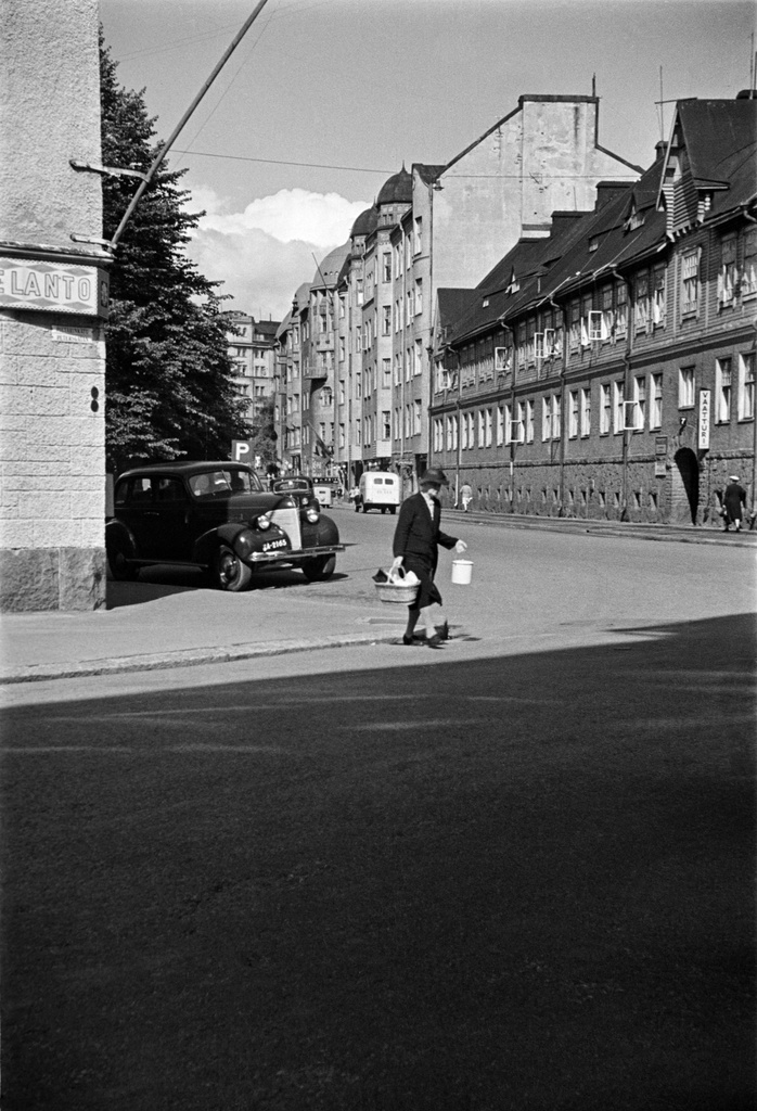 Näkymä Pietarinkadulta pohjoiseen pitkin Kapteeninkatua, oikealla Kapteeninkatu 7, 9. Etualalla nainen ylittää katua, vasemmalla talon seinässä Elannon kyltti, oikealla vaatturiliike.