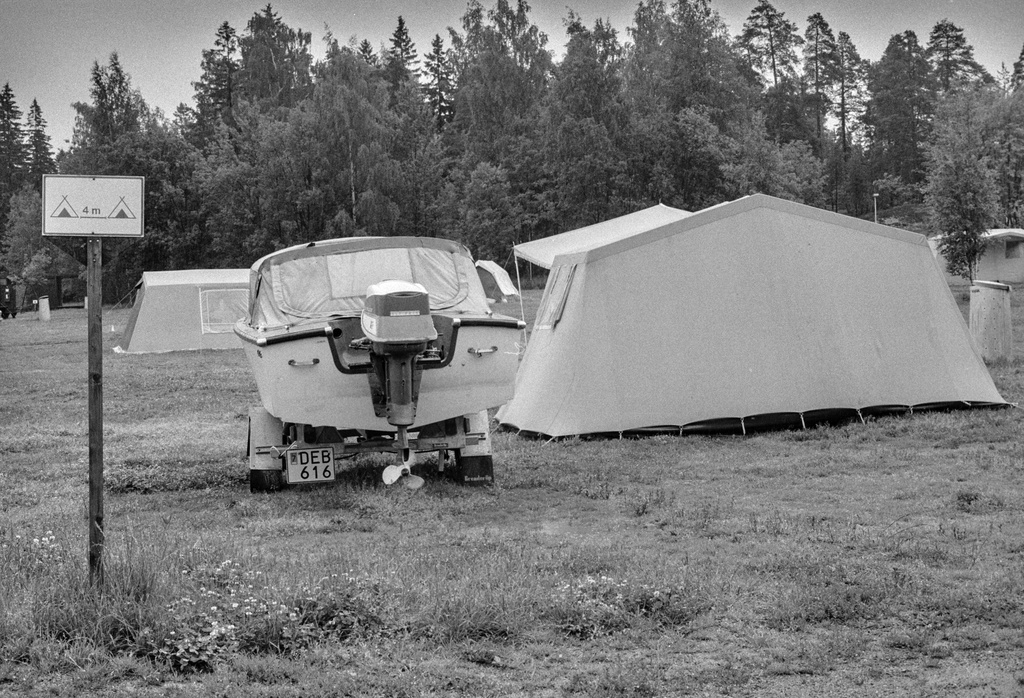 Rastila Camping leirintäalue. Leirintäalueelle pystytettyjä telttoja. Opaskyltti, jossa neuvotaan jättämään neljä metriä tilaa pystytettyjen telttojen väliin. Kyltin ja teltan välissä on kuljetusalustalla oleva moottorivene.