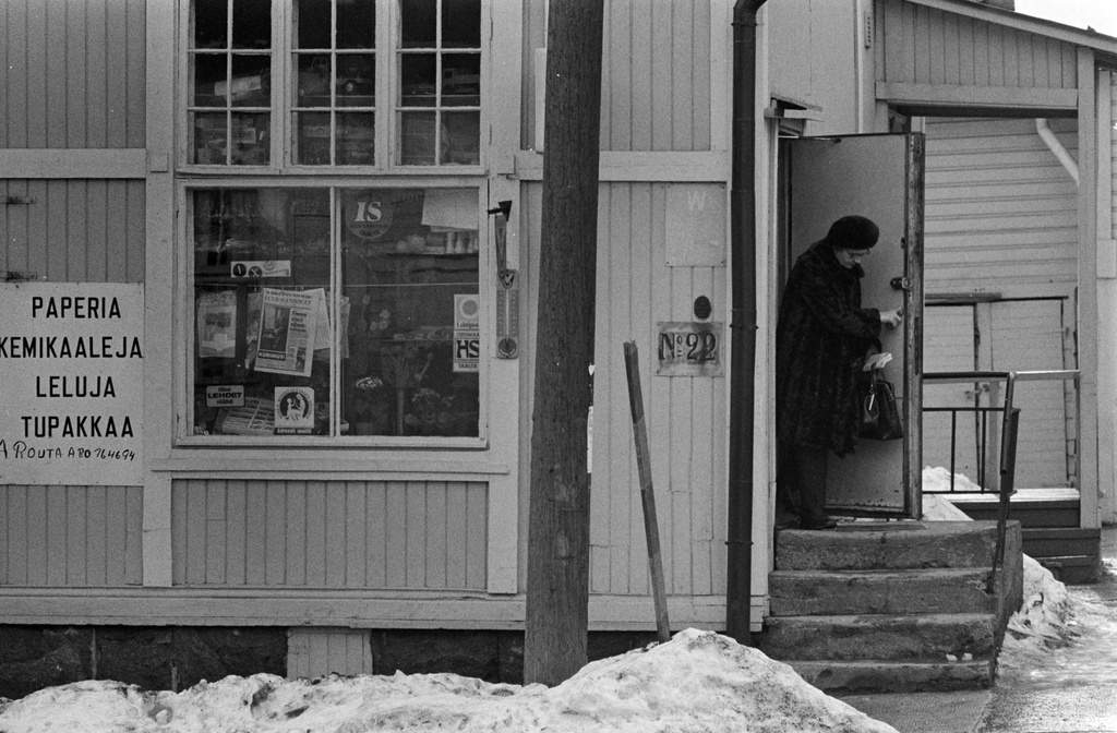 Paperi-, kemikaali-, lelu- ja tupakkakauppa A. Routa-Aro puutalossa Vallilantiellä Puu-Vallilassa. Liikkeen ulko-ovesta on tulossa ulos nainen.