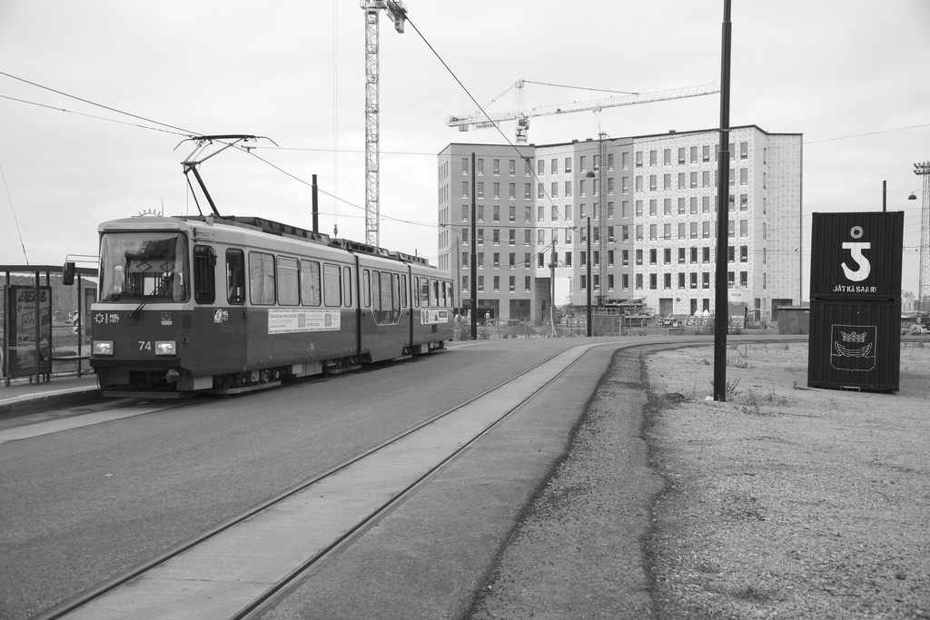 Jätkäsaaren dokumentointi. Raitiovaunu 8 päätepysäkki, taustalla Atlantinkatu 7. Oikealla musta kontti, jossa Jätkäsaaren logo (nosturin koukku), Helsingin vaakuna ja teksti: "Jätkäsaari".