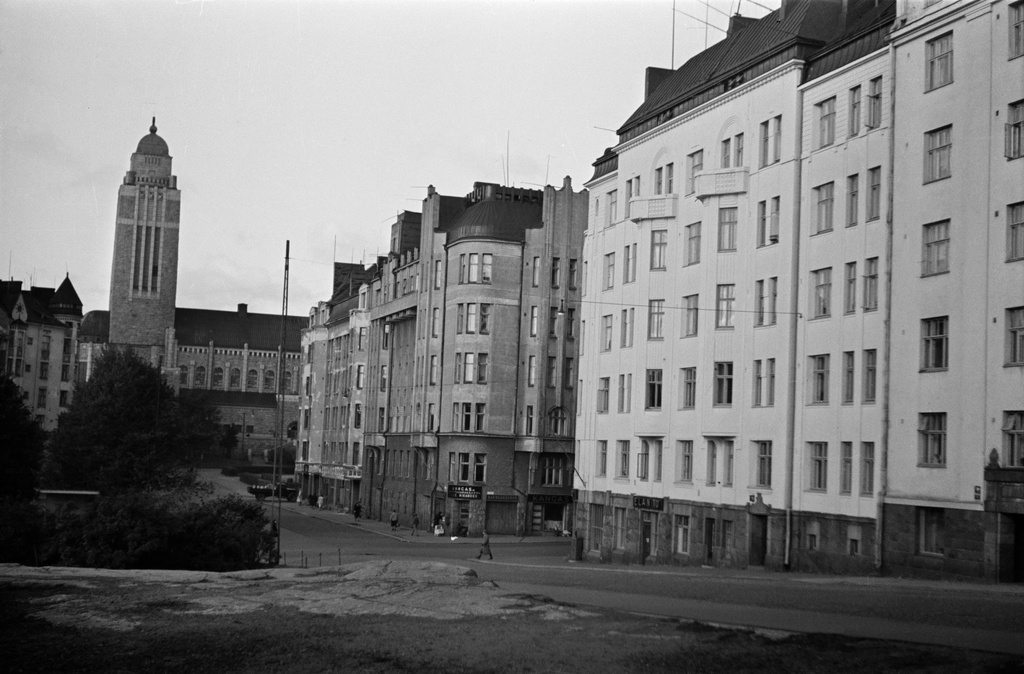 Agricolankatu 7, 9, 11 (=Fleminginkatu 2), 13. Taustalla Kallion kirkko, vasemmalla Karhupuisto. Kulmassa keskellä kangas- ja lyhyttavarakauppa J. E. Nikander.