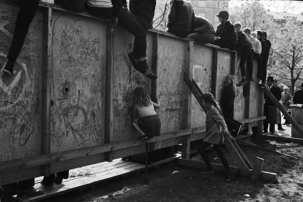 Karhupuisto. Helsingin juhlaviikot. Lapsia kurkistelemassa näyttämön taustarakennelman rei'istä muusikko Jukka Kuoppamäen esiintymistä puistotapahtumassa Karhupuistossa.
