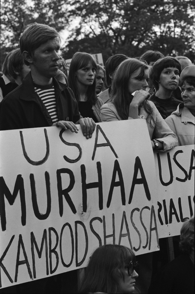 Kaisaniemenpuisto. Ihmisiä kyltteineen Vietnamin sodan vastaisessa mielenosoituksessa Kaisaniemenpuistossa. Kyltissä teksti: USA murhaa Kambodshassa.