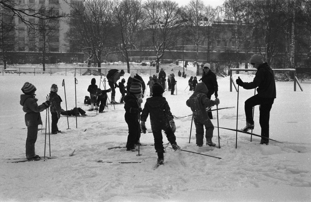 Kaisaniemenpuisto. Vironniemen päiväkodin lapset ja aikuiset lumisessa Kaisaniemenpuistossa valmistautumassa lähtöön hiihtoretkelle. Näkymä Unioninkadun suuntaan.
