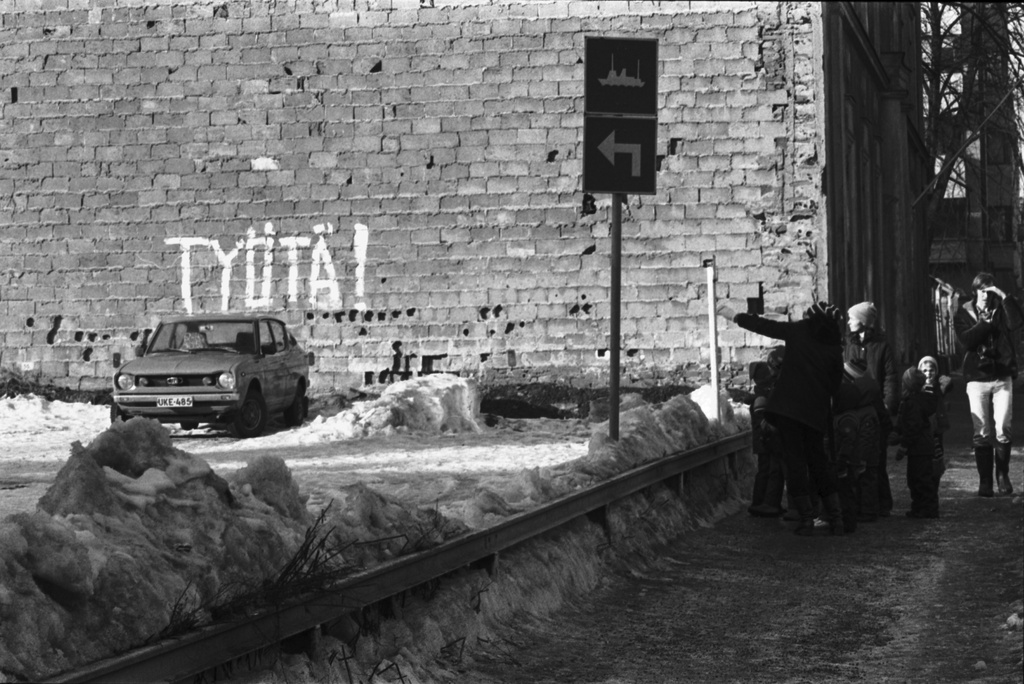 Kirkkokatu 4. Vironniemen päiväkodin lapsia ja opettajia Kirkkokatu 4:n rakentamattoman tontin kohdalla. Taustalla Kirkkokatu 6:n talon tiilipäädyn seinässä teksti TYÖTÄ!.