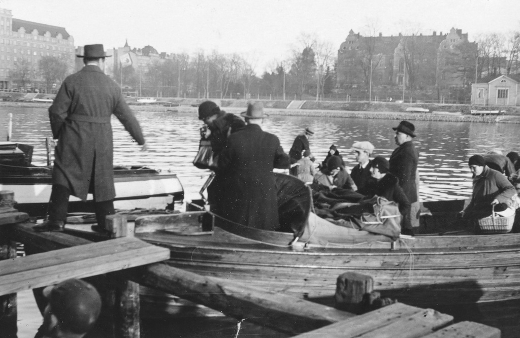 Helsingin Työväenyhdistyksen Sekakuoron jäseniä palaamassa veneellä Herttuasta Siltasaaren rantaan keväällä 1930-luvun alussa. Taustalla Unioninkatu, Kaisaniemenranta ja Kasvitieteellinen puutarha.