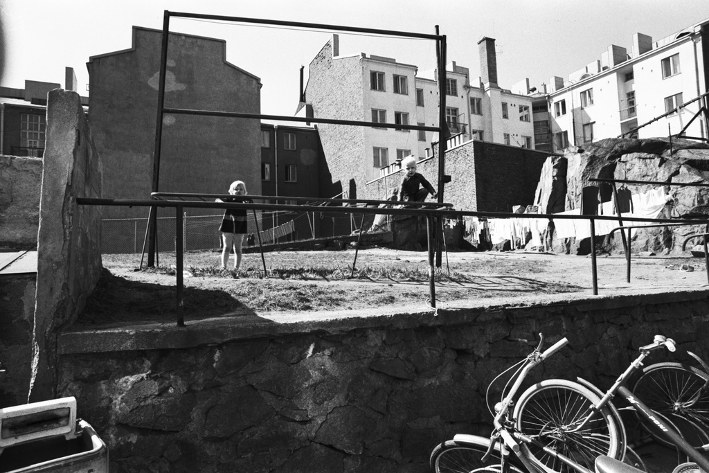 Fleminginkatu 14. Näkymä Fleminginkatu 14:n pihalta. Lapsia matontamppaustelineellä, etualalla polkupyöriä, taustalla kerrostaloja.