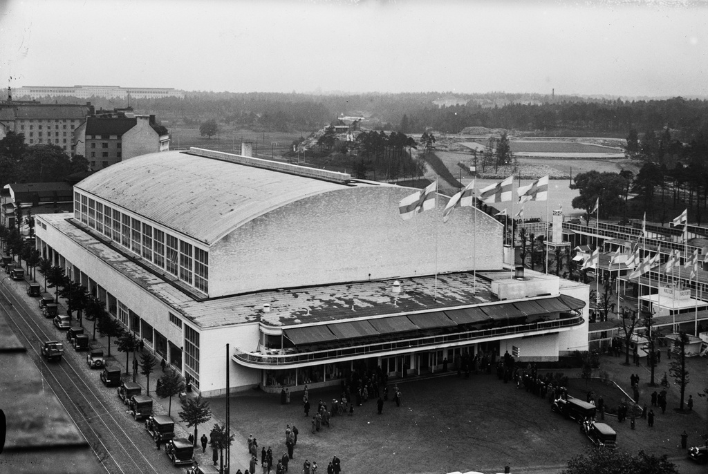 Suurmessut 1935 Helsingin messuhallissa. Yleisnäkymä messualueelle ja messuhalliin, jonka päälle on satanut hento lokakuinen lumisade. Taustalla vasemmalla 1930 toimintansa aloittanut Helsingin tuberkuloosisairaala eli Laakson sairaala. Oikealla metsän keskeltä erottuu nykyisin Auroran sairaalana tunnettu lastensairaala, joka oli perustettiin vuonna 1914 Helsingin kunnalliseksi kulkutautisairaalaksi. Sen ja messuhallin välissä oleva tasoitettu alue on tulevan Helsingin Olympiastadionin rakennustyömaan pohja. Suurmessut olivat vuonna 1935 valmistuneen messuhallin ensimmäinen messutapahtuma.