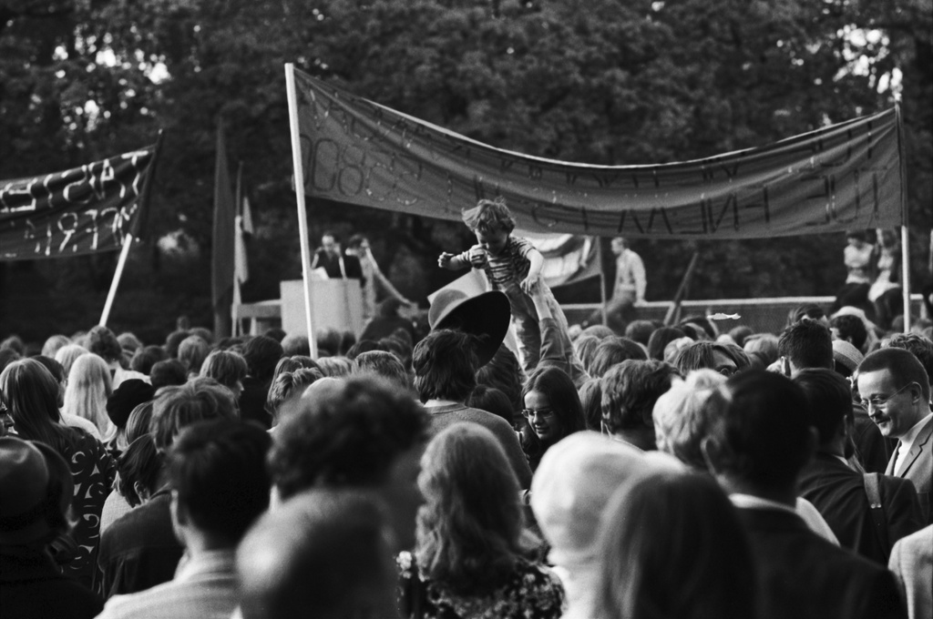 Kaisaniemenpuisto. Vietnamin sodan vastaisen mielenosoitusmarssin päätepisteeseen kokoontuneita ihmisiä banderolleineen Kaisaniemenpuistossa. Keskellä lapsi päiden yläpuolella.