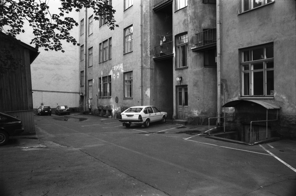 Rauhankatu 13. Näkymä Rauhankatu 13:n pihalta idän suuntaan. Vasemmalla piharakennus, oikealla sisäänkäynti A-portaaseen. Pihalla pari autoa.