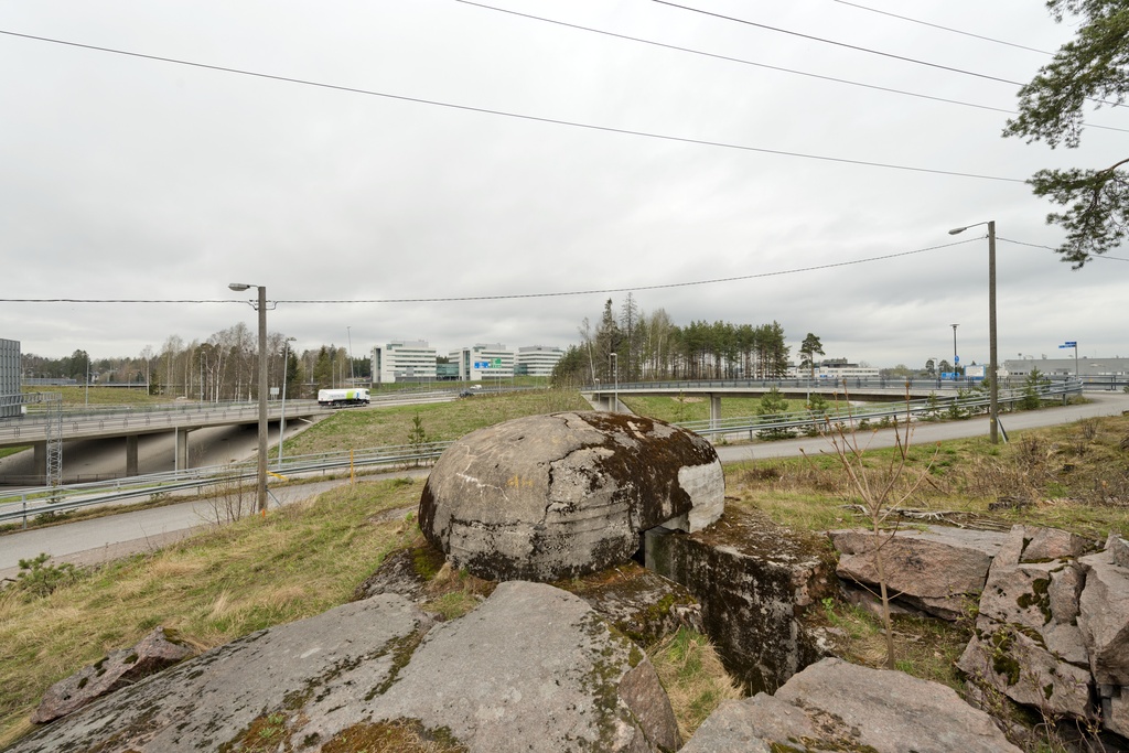 Ruukinranta. Ensimmäisen maailmansodan aikainen maalinnoitus, puolustusasema XXXVI:2 Ruukinrannassa, Espoossa. Kuvassa on linnoitteen länsipäässä sijaitseva pyöreä, kupukattoinen kivääri- tai tähystysasema. Betonisen rakenteen päällyskupu siirrettiin 1970- luvulla tietöiden yhteydessä puolustusasemasta XXXVI:1 tälle paikalle, jossa oli samanlaisen, keskeneräiseksi jääneen aseman alaosa valmiina. Asemaan johtaa kallioon louhittu, keskeneräiseksi jäänyt hauta. Taustalla näkyy Kehä 1:n ja Turunväylän välinen risteyssilmukka, sekä risteyksen luoteispuolella sijaitsevia rakennuksia. Kuvaussuuntana pohjois-luode.