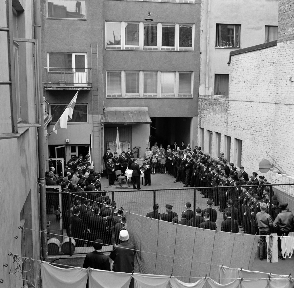 Helsingin vapaapalokunnan (VPK, FBK) vuosikokous Albertinkatu 29-31:n sisäpihalla, palkintojen jako, ympärillä yleisöä. Etualalla pyykkiä kuivumassa.