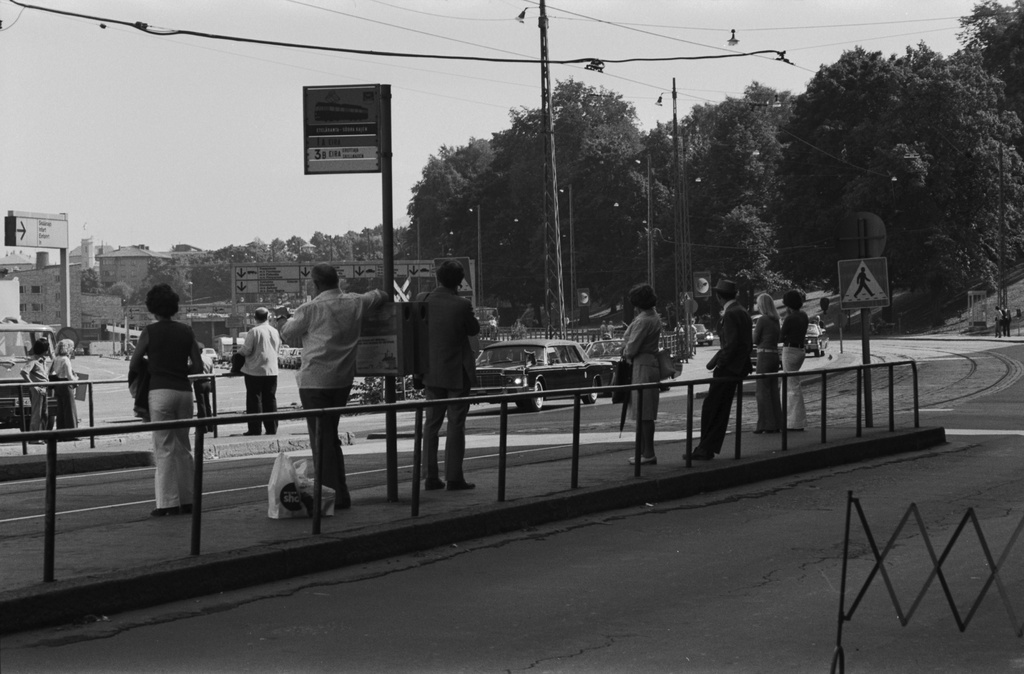 Eteläranta. Valtiomiesten autoja poliisisaattueessa Etelärannassa. Etualalla raitiovaunupysäkillä ihmisiä seuraamassa tapahtumaa. Euroopan turvallisuus- ja yhteistyökokous (ETYK) järjestettiin Helsingissä Finlandia-talossa heinä-elokuun vaihteessa 1975.