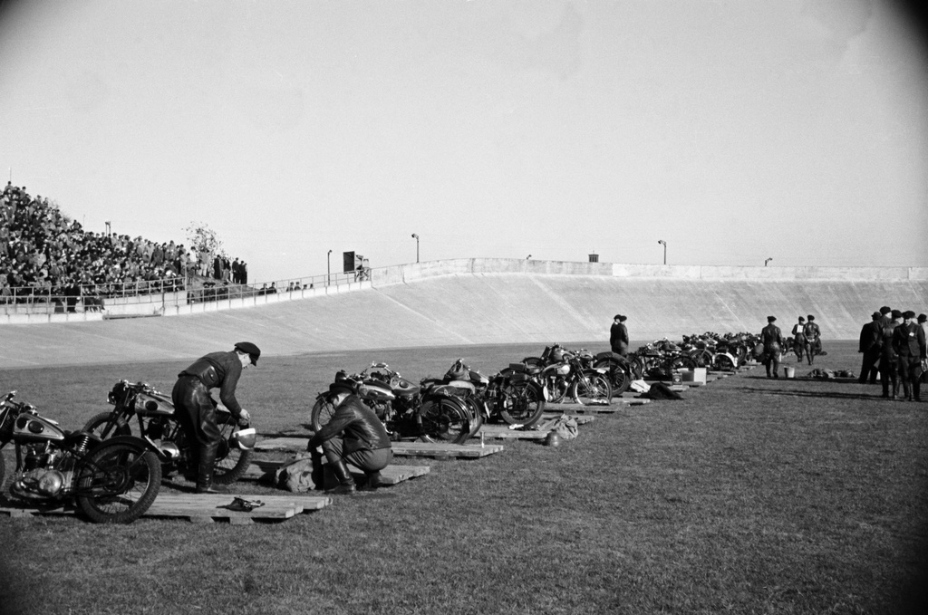 Velodrom, Helsingin pyöräilystadion, moottoripyöräkilpailut. Kilpailijoita ja moottoripyöriä radan reunassa, vasemmalla katsomo ja yleisöä.